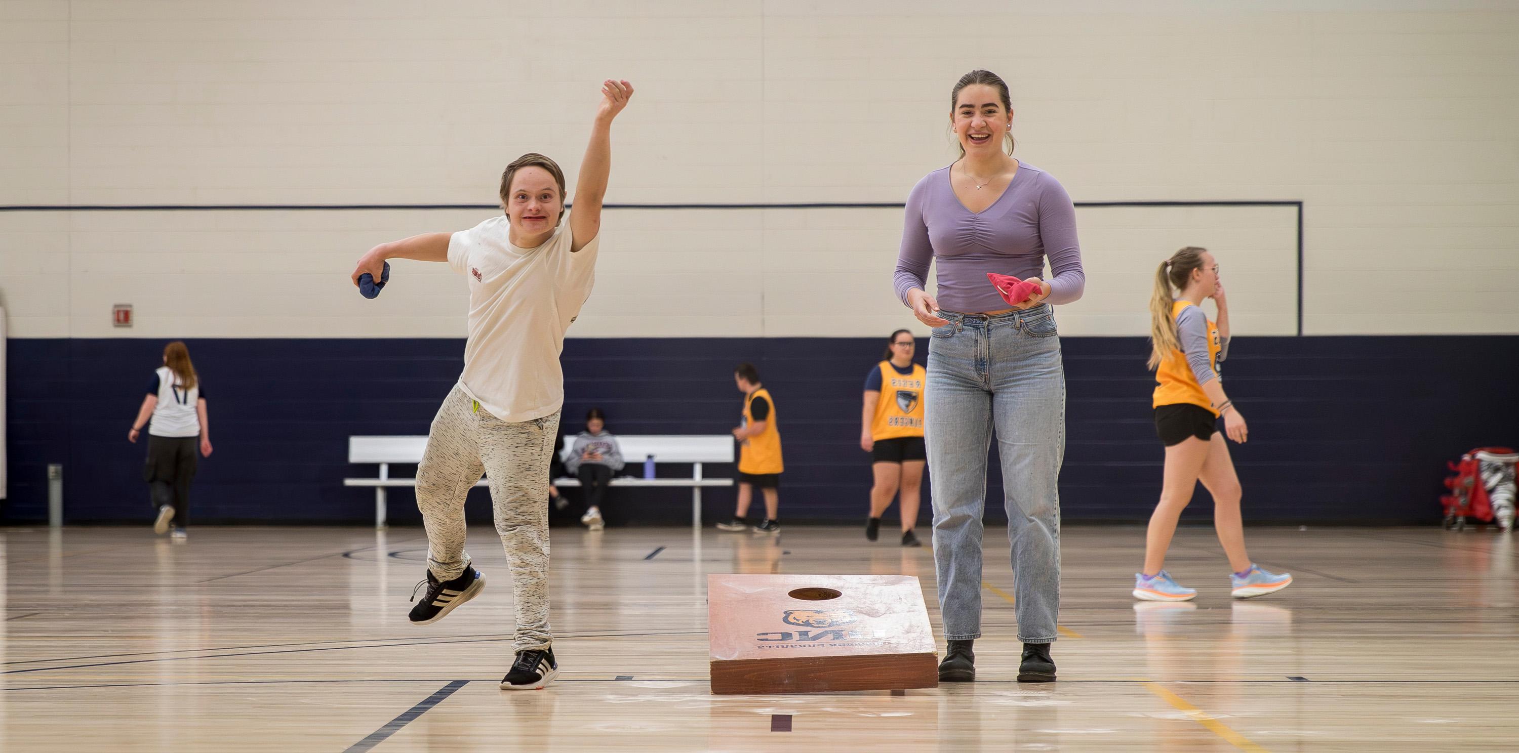 Two people standing next to each other, one is tossing a bag